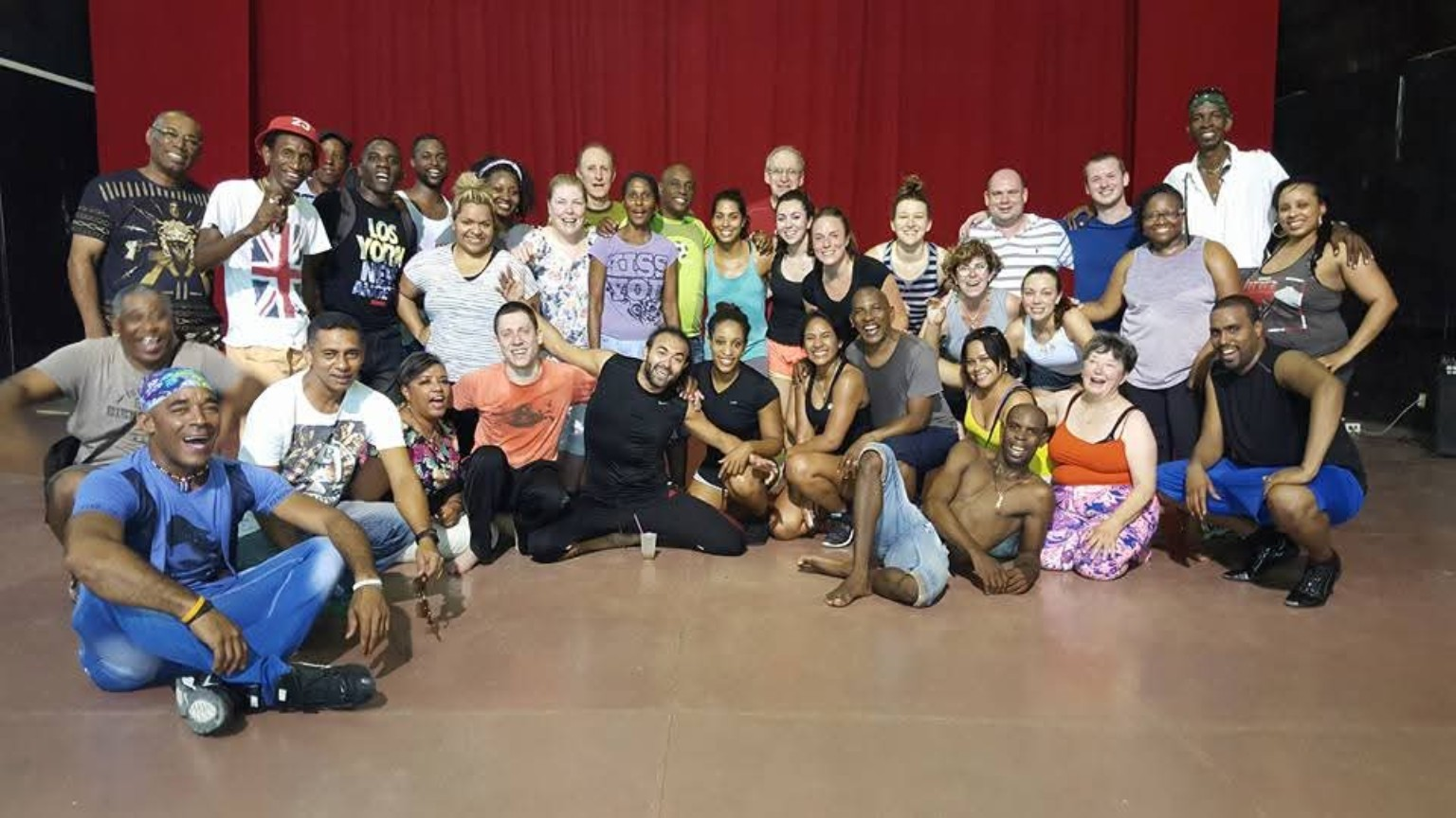DC Casineros and students gathered with Folklórico Cutumba dancers in front of a red studio curtain in Santiago de Cuba