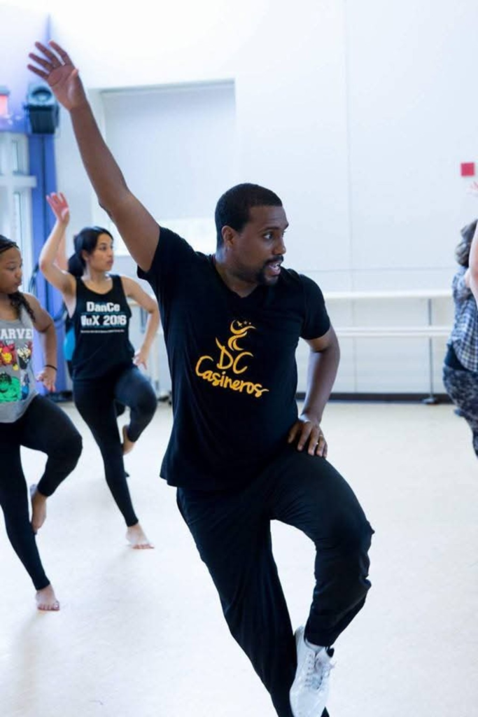 A DC Casineros teaching artist demonstrating a raised-arm movement in a dance class.