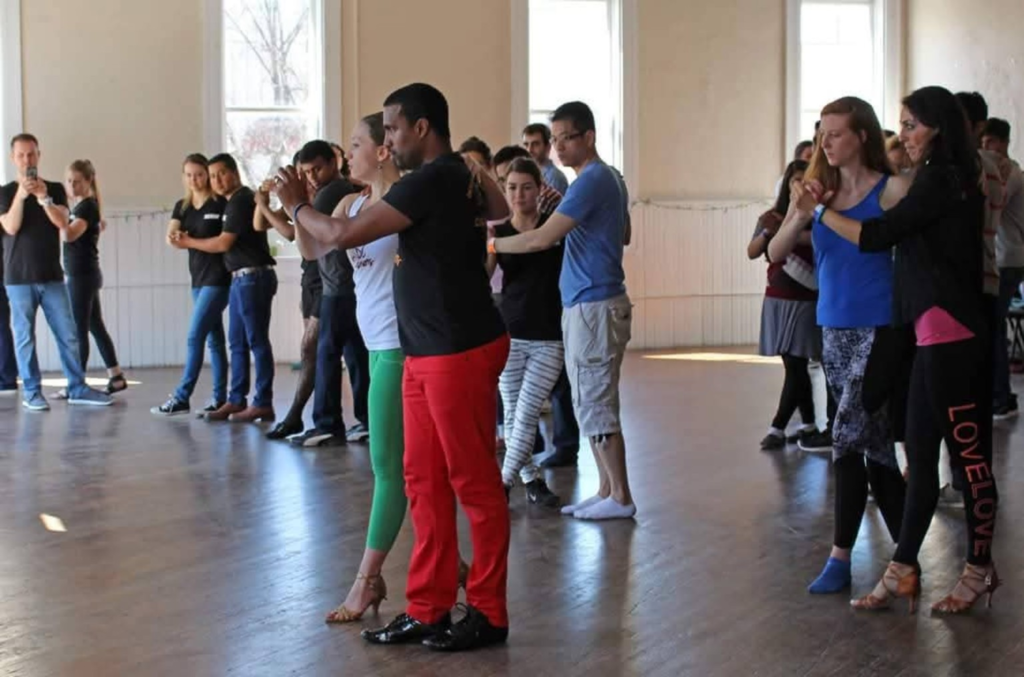 Participants practicing partner dance together in a bright classroom.
