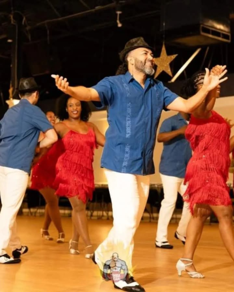 A DC Casineros performer in a blue shirt and hat dancing with the ensemble.