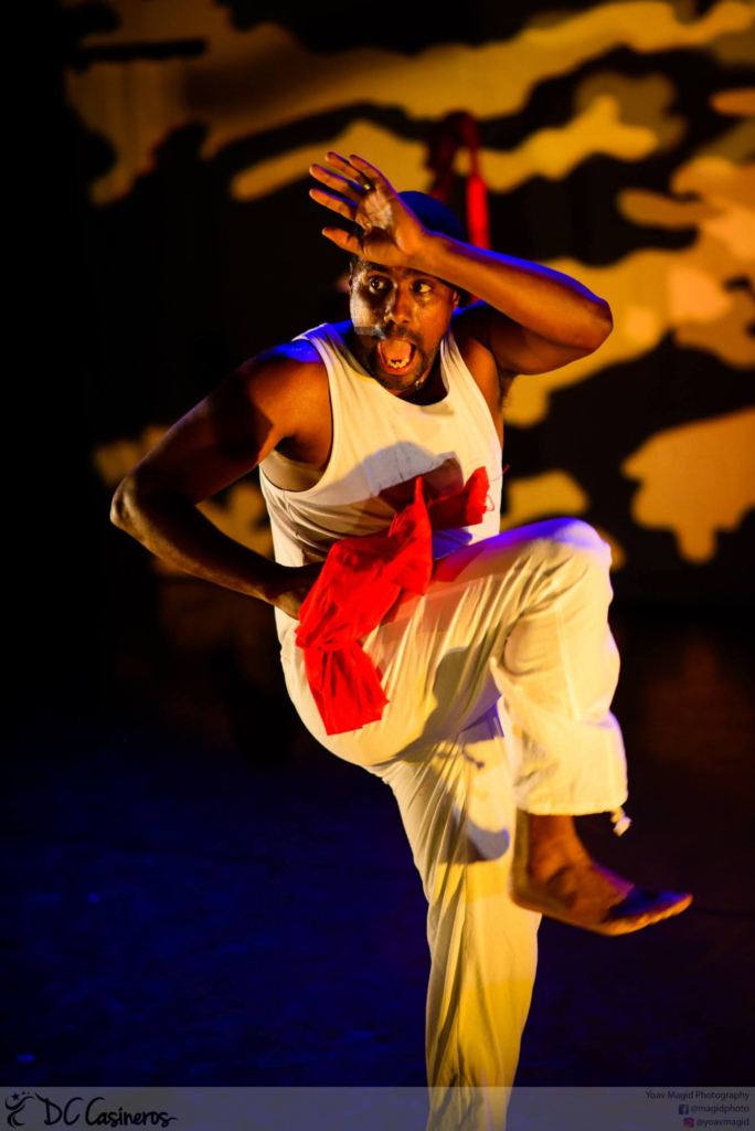 A DC Casineros dancer in white performing a dynamic solo under gold and blue stage lighting