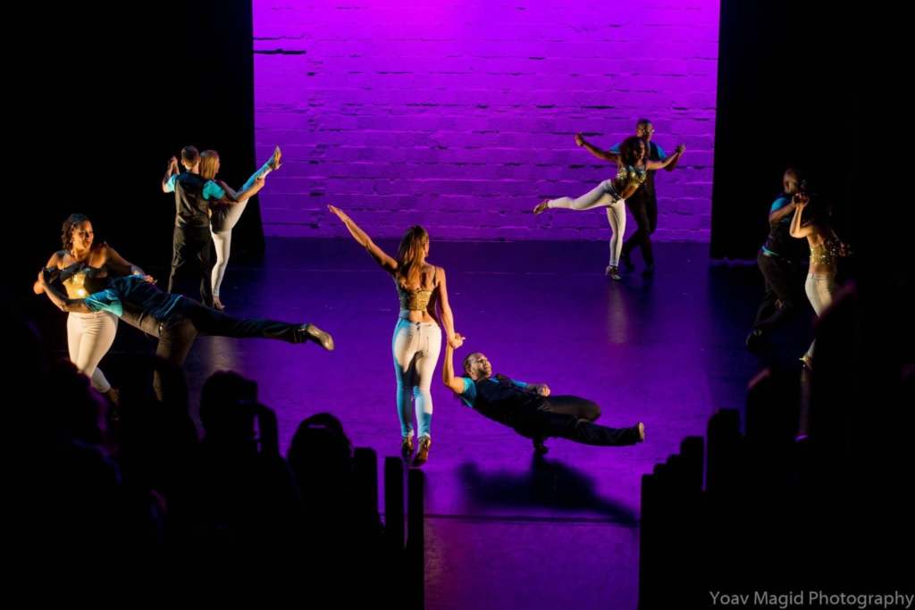 DC Casineros ensemble performing synchronized partner balances on a purple-lit theater stage.