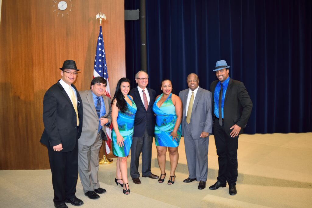 DC Casineros dancers in blue costumes with hosts on a State Department stage in 2015